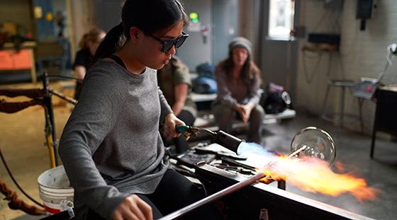 person working with glass while a group watches